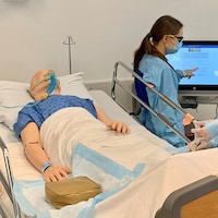 Deux étudiants en soins infirmiers portant des masques d'intervention travaillent avec un mannequin sur un lit d'hôpital.