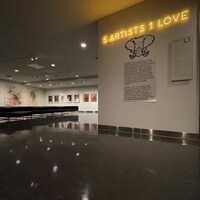 Une salle du musée où il est écrit en néon 5 Artists 1 Love. Sur un autre mur, au fond de la salle, on aperçoit des cadres.