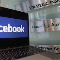 Un ordinateur portable montrant le logo de Facebook est posé à côté d'une plaque indiquant les bureaux de Cambridge Analytica, à Londres.