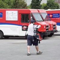 Un postier passe devant les camions de Postes Canada dans un centre de tri.