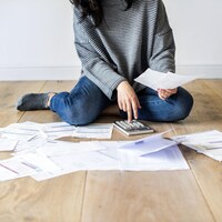 Une femme, qui utilise une calculatrice, a des factures au sol.
