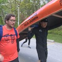 Félix Jasmin marche avec un coéquipier en portant son canot.