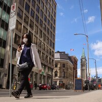 Une femme portant un masque chirurgical marche sur un trottoir du centre-ville d'Ottawa.