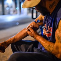 Un homme s'injecte de l'héroïne dans la rue, la nuit.