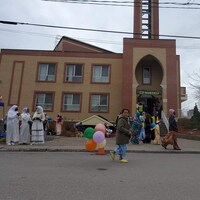Des gens rassemblés devant une mosquée. Au premier plan, un enfant passe avec des ballons.
