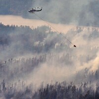 Un hélicoptère survole une forêt remplie de fumée.