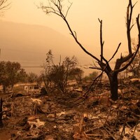 Une épaisse fumée remplit l'air et bloque presque le soleil alors qu'une propriété détruite par un incendie de forêt est vue à Monte Lake, en Colombie-Britannique, en août 2021.