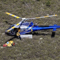Photo aérienne d'un hélicoptère bleu posé au sol. Un individu s'apprête à y monter.