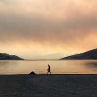 Une personne qui marche sur la plage sous un ciel rouge et brumeux.