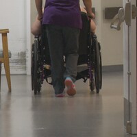 Une préposée aide un résident à se déplacer en fauteuil roulant dans un couloir du foyer de soins.
