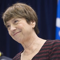 Françoise David en gros plan sourit alors qu'elle est est posée devant un drapeau du Québec. 