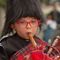 Frankie Whelan, en habit écossais traditionnel complet, kilt et bonnet de plumes compris, joue de la cornemuse.
