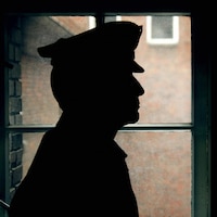 Un gardien de prison, portant une casquette, de profil dans l'ombre.