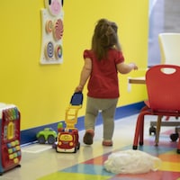 Une petite fille, de dos, dans une garderie et traîne un jouet.