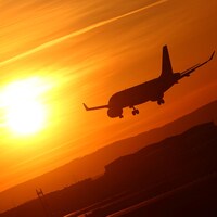 Silhouette d'un avion de ligne qui descend vers la piste dans le soleil couchant.