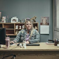 Une femme est assise à son bureau de travail, qui est orné de plusieurs animaux en porcelaine. 