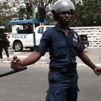 Un policier en uniforme et casqué tient une matraque dans sa main droite.
