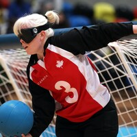 Une femme avec des lunettes qui cachent ses yeux et tient le filet de but et le ballon. 