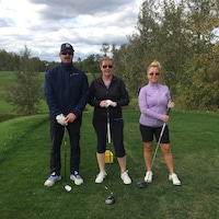 Trois golfeurs, un homme et deux femmes, au milieu d'un terrain de golf.