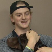Un jeune homme portant une casquette à l'envers serre un chien dans ses bras.