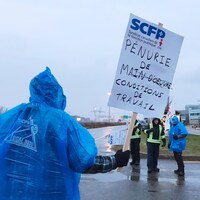 Un gréviste tient une pancarte où il est inscrit : « Pénurie de conditions de travail ».