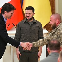 Le premier ministre du Canada, Justin Trudeau, serre la main d'un militaire alors que le président de l'Ukraine Volodymyr Zelensky sourit à l'arrière-plan en regardant M. Trudeau.