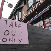 Une affiche dit « mets à emporter seulement » devant un restaurant.