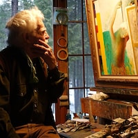 Henry Wanton Jones assis devant son chevalet regarde une peinture.