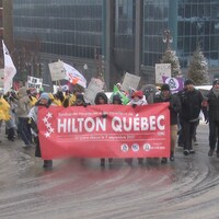 Pancartes à la main, des manifestants agitent une banderole en appui aux grévistes du Hilton Québec. Ils défilent dans une rue de Québec.