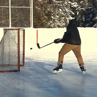 Un homme un lancer dans un filet de hockey sur une patinoire extérieure.