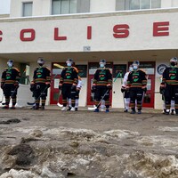 Les joueurs de l'équipe de hockey Les Patriotes vêtus de leur équipement posent devant le colisée de Trois-Rivières