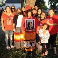 Un groupe de personnes debout avec une femme qui tient la photo en cadre de la victime d'un homicide.