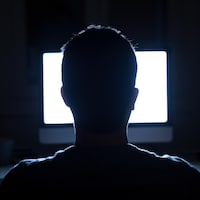 Silhouette d'un homme devant la lumière d'un écran d'ordinateur dans la pénombre.