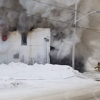 Des pompiers tentent d'éteindre un incendie, alors qu'un épais panache de fumée se dégage d'un bâtiment.
