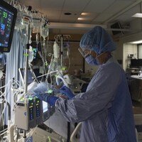 Une infirmière dans un hôpital, à côté d'un patient sous aide respiratoire.