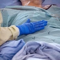 Une infirmière pose une main gantée sur le ventre d'un patient.