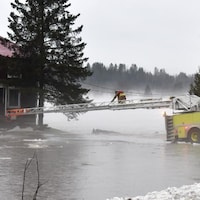 Un pompier sur une échelle s'avance vers une maison inondée