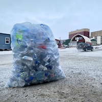 Un sac contenant des bouteilles de plastique vides est posé au sol dans une rue d'Iqaluit.