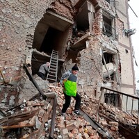 Une femme transporte un sac dans les ruines d'un immeuble éventré.