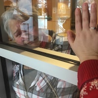 La grand-mère a le visage écrasé contre la vitre. Elle y appose sa main et sa petite-fille met sa main au même endroit. 