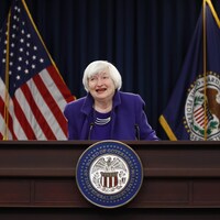 Janet Yellen est derrière un lutrin portant le sceau de la Fed, et devant des drapeaux des États-Unis et de la Fed.