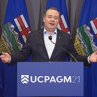 Jason Kenney écarte les bras en s'adressant aux médias.