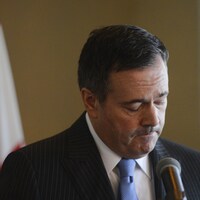 Le premier ministre albertain Jason Kenney, tête baissée et l'air préoccupé, parle au micro.