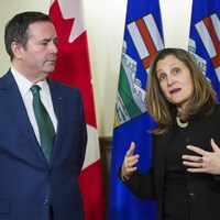 Jason Kenney, mains dans le dos, semble attentif à ce que dit Chrystia Freeland, à ses côtés.