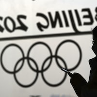 Une femme regarde son téléphone devant un logo des Jeux olympiques de Pékin.