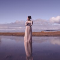 La chanteuse se tient debout dans l'eau, sur le bord du fleuve Saint-Laurent. Elle porte une longue robe pâle. 
