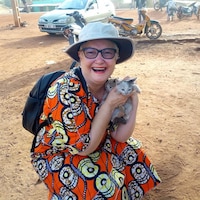 José Leclair, en boubou africain, tout sourire, tient des bébés chats dans ses mains.