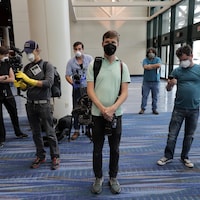 Sept représentants des médias portant de l’équipement de protection comme des gants et des masques attendant dans un hall.