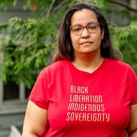 Joy Henderson regarde la caméra. Elle porte un t-shirt rouge sur lequel est écrit «Black Liberation Indigenous Sovereignty».