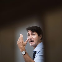 Gros plan de Justin Trudeau qui lève la main gauche en regardant au loin.